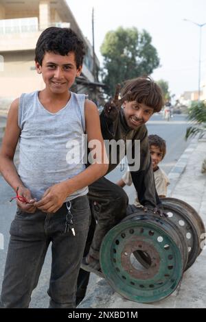 Focalizzazione selettiva sui bambini lavoratori siriani nel negozio di riparazione auto. I bambini con mani e vestiti sporchi sorridono. Uno di loro sta facendo un segno di vittoria. Foto Stock