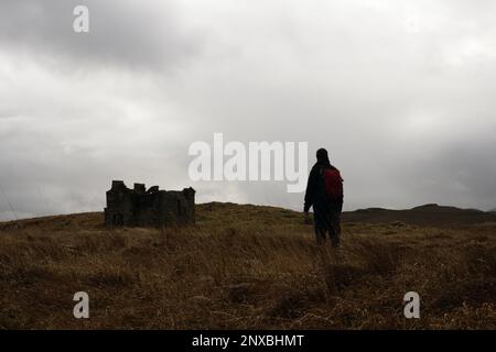 Un escursionista, di nuovo alla macchina fotografica. Guardando ad una casa misteriosa abbandonata, in rovina. Su una collina desolata e spooky. In inverno. Foto Stock