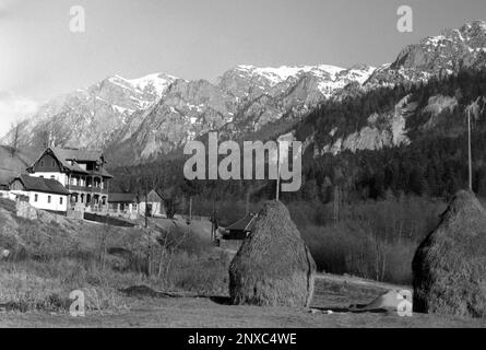 Valle di Prahova, Romania, circa 1974. Paesaggio con i Monti Bucegi in primavera, case di montagna e fienili in un pascolo. Foto Stock