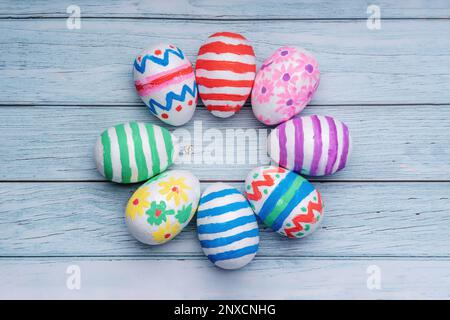 Colorate uova di Pasqua disposte in un motivo circolare su uno sfondo di legno blu pastello, creando uno spazio perfetto per i messaggi e i saluti di Pasqua Foto Stock