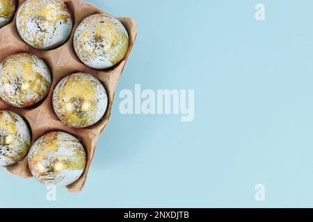 Uova di Pasqua dipinte con macchie dorate in scatola di uova su sfondo blu con spazio copia Foto Stock