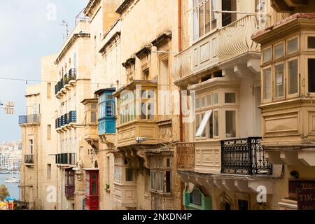 Valletta, Malta - 12 novembre 2022: Facciate residenziali in pietra calcarea intemperate con tradizionali balconi in legno nella capitale di Malta Foto Stock