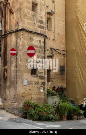 La Valletta, Malta - 11 novembre 2022: Calcarea casa d'angolo con due segnali stradali vietati che indicano la direzione sbagliata e piante pentola nel marciapiede Foto Stock