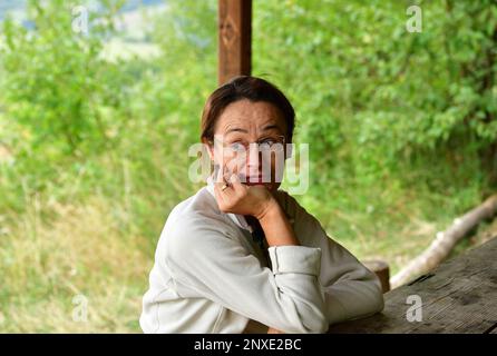 Un escursionista femminile si siede e riposa in una casa di legno durante un'escursione nella foresta Foto Stock