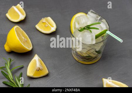 Bicchiere di bevanda estiva con ghiaccio e limone. Fette di limone sul tavolo. Giacitura piatta. Sfondo grigio. Foto Stock