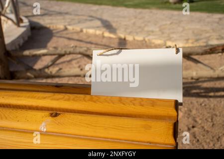 su un cartello bianco appeso al banco del parco con spazio libero vuoto per il modello o l'area di copia vuota Foto Stock