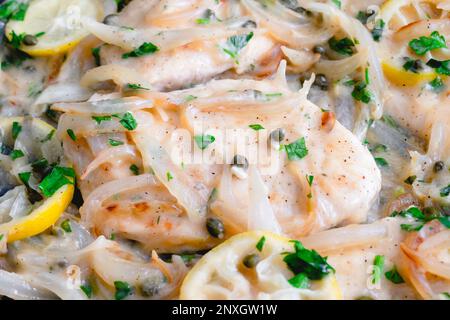 Vista ravvicinata di cipolle a fette inaronate in uno Skillet: Cotolette di pollo e fettine di limone cucinate in una salsa di vino bianco con capperi Foto Stock