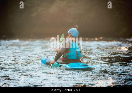 Atleta sportivo maschile che si addica con attenzione sulle rischiose, schiumose rapide e spruzzi nel suo kayak blu Foto Stock