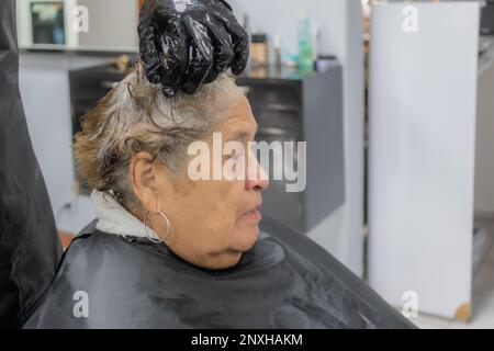Capelli massaggianti capelli corti della donna anziana con tintura su sfondo sfocato, espressione seria, vista laterale. Moda antica e bellezza concep
