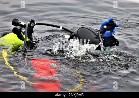 Un vigile del fuoco con la direzione dei servizi di emergenza del team di immersione del Dipartimento dei vigili del fuoco pratica uno scenario di salvataggio su ghiaccio 11 gennaio 2023, presso un lago congelato Big Sandy sul South Post a Fort McCoy, Wisconsin. Diversi vigili del fuoco con la squadra hanno preso il loro turno, indossando un vestito, reggendo un serbatoio dell'aria e una maschera a pieno facciale, e tuffandosi nelle profondità del lago Big Sandy sotto il ghiaccio sul South Post di Fort McCoy. I subacquei stavano coprendo profondità fino a 15 piedi o più completando diversi tipi di scenari di salvataggio sotto la guida di altri vigili del fuoco. I subacquei hanno preso i giri che vanno dentro e fuori dello stesso foro che è stato tagliato Foto Stock