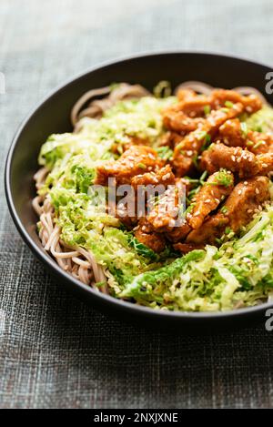 Ricci di soia piccanti su cavolo sminuzzato di savoia, serviti con spaghetti di grano saraceno. Foto Stock