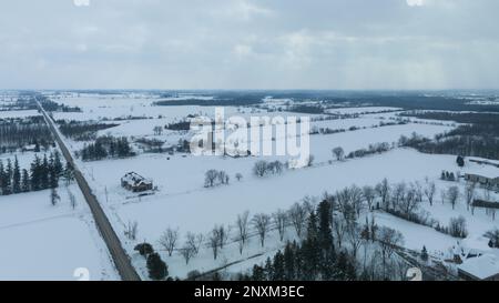 Un vasto paesaggio rurale coperto di neve è visto da una vista aerea ad alto angolo nelle giornate nevose; case, fattorie sono viste in lontananza. Foto Stock