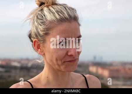 Ritratto di una donna bionda, bella, matura con occhi verdi in una t-shirt nera e acconciatura con un arco sullo sfondo della città di Madrid Foto Stock