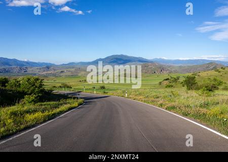 Winding tarmac road through Mtkvari river valley in Samtskhe - Javakheti region, Georgia with green fields around and Lesser Caucasus mountains. Foto Stock