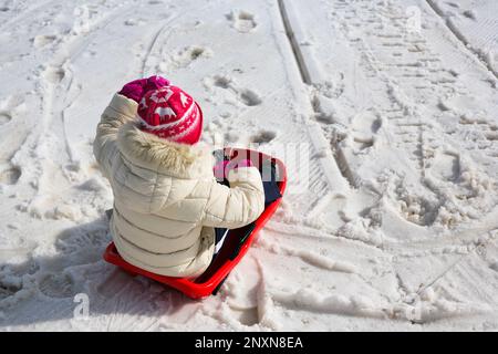 Una bambina sta slittando su una slitta rossa Foto Stock