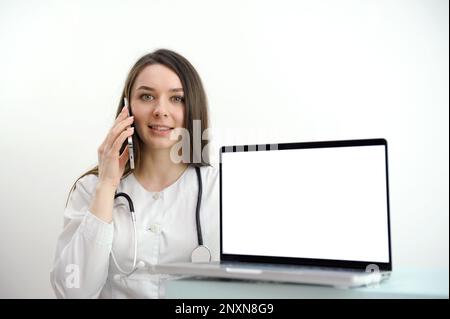 L'assistente medico femminile indossa un cappotto bianco, videochiama un paziente distante sul computer portatile. Medico che parla con il cliente utilizzando l'app per computer di chat virtuale. Telemedicine, concetto di servizi sanitari a distanza Foto Stock