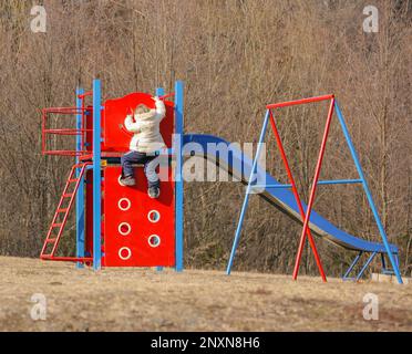 Una bambina in un parco per bambini si arrampica su una roccia artificiale Foto Stock