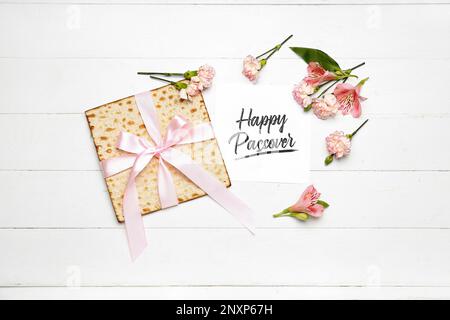 Scheda con testo HAPPY PASSOVER, pane piatto mata e fiori di alstroemeria su sfondo di legno chiaro Foto Stock