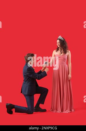 Giovane uomo che legava il corsage intorno al polso della sua data di prom su sfondo rosso Foto Stock