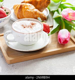 Buona giornata della mamma, bella colazione, pranzo con tazza di caffè (cappuccino) cornetti freschi, fragole su vassoio, bouquet di tulipani in regalo. Foto Stock