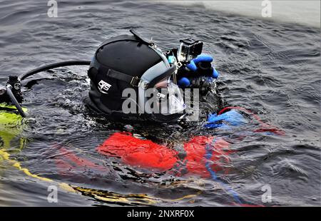 Un vigile del fuoco con la direzione dei servizi di emergenza del team di immersione del Dipartimento dei vigili del fuoco pratica uno scenario di salvataggio su ghiaccio 11 gennaio 2023, presso un lago congelato Big Sandy sul South Post a Fort McCoy, Wisconsin. Diversi vigili del fuoco con la squadra hanno preso il loro turno, indossando un vestito, reggendo un serbatoio dell'aria e una maschera a pieno facciale, e tuffandosi nelle profondità del lago Big Sandy sotto il ghiaccio sul South Post di Fort McCoy. I subacquei stavano coprendo profondità fino a 15 piedi o più completando diversi tipi di scenari di salvataggio sotto la guida di altri vigili del fuoco. I subacquei hanno preso i giri che vanno dentro e fuori dello stesso foro che è stato tagliato Foto Stock