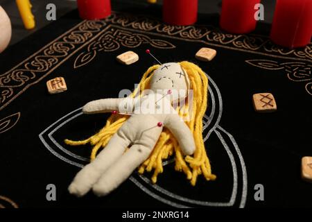 Voodoo bambola trafitto con spilli e rune sul tappeto nero. Maledizione cerimonia Foto Stock