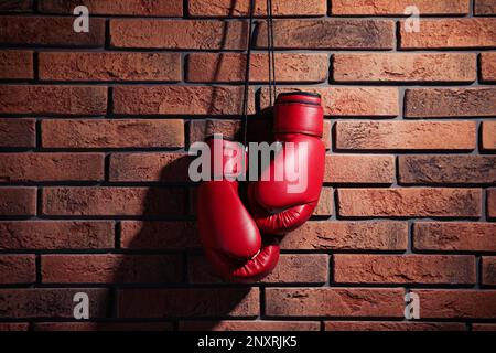 Coppia di guanti da boxe rossi appesi su parete in mattoni Foto Stock