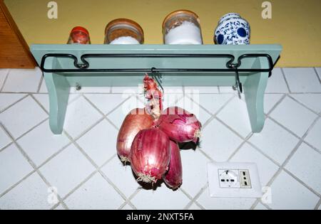 Cucina italiana: Una treccia di cipolline rosse dolci tropea appese in cucina Foto Stock