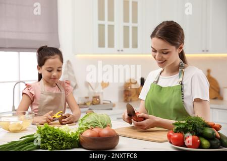 Madre e figlia che pelano le verdure al tavolo in cucina Foto Stock