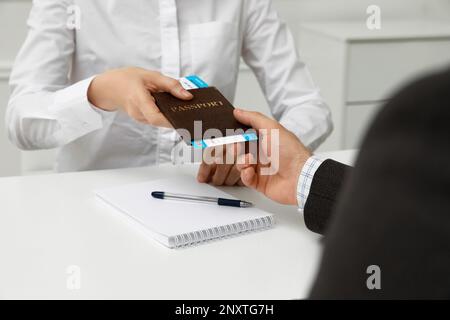 Manager che fornisce il passaporto e il biglietto per l'uomo alla scrivania presso l'ufficio dell'agenzia di viaggi, in primo piano Foto Stock