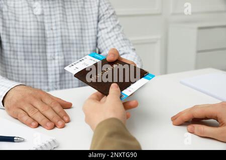 Manager che fornisce il passaporto e il biglietto per l'uomo alla scrivania presso l'ufficio dell'agenzia di viaggi, in primo piano Foto Stock