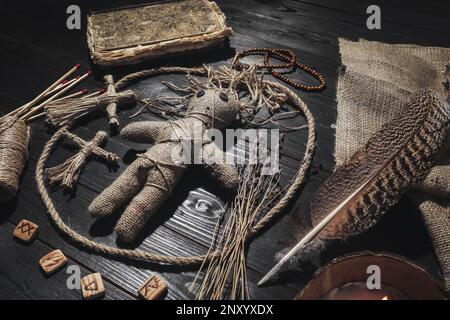 Bambola voodoo femminile con spille circondate da oggetti cerimoniali su sfondo di legno nero Foto Stock
