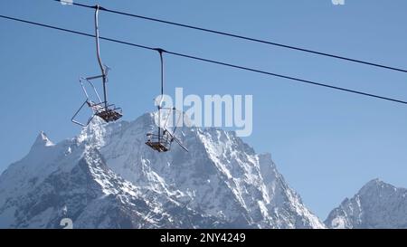 Funivia sullo sfondo delle cime di montagna e cielo blu. Creativo. Montacarichi con cabine mobili vuote con montagne innevate. Bellissimo paesaggio Foto Stock