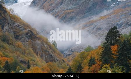 Paesaggio montano con nuvole basse che si muovono nella valle. Creativo. Valle autunnale con pendici rocciose e nuvole in movimento. Misty nuvole basse misterioso Foto Stock