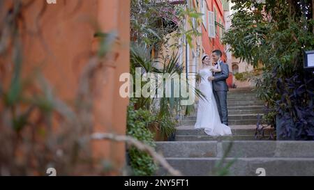 Sposi novelli che scattano foto per strada. Azione. Una giovane coppia con una sposa in un vestito bianco e un uomo in una tuta che sono fotografati in piena altezza Foto Stock