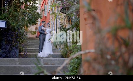 Sposi novelli che scattano foto per strada. Azione. Una giovane coppia con una sposa in un vestito bianco e un uomo in una tuta che sono fotografati in piena altezza Foto Stock