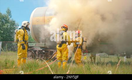Vigili del fuoco e treno in fiamme. Fermo. I vigili del fuoco si stanno preparando con attrezzature per spegnere gli incendi. Predisposizione per lo spegnimento di un vagone ferroviario industriale Foto Stock