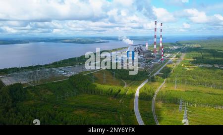 Vista aerea della zona industriale della città e di un ampio fiume. Fermo. Volare sopra la foresta estiva e una centrale elettrica su uno sfondo cielo luminoso Foto Stock
