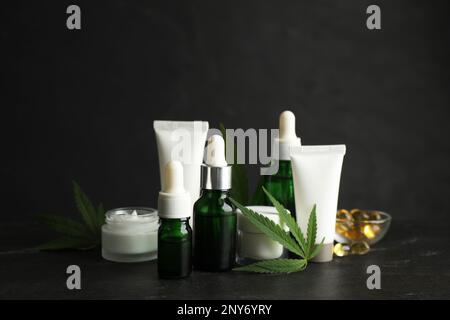 Composizione con olio CBD, tintura di THC e foglie di canapa su tavola di pietra nera Foto Stock