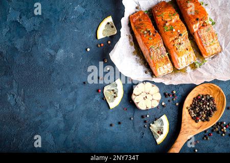 Delizioso filetto di salmone fritto con condimenti su fondo di cemento rustico blu. Bistecca di salmone cotta con pepe, erbe aromatiche, limone, aglio, cucina Foto Stock