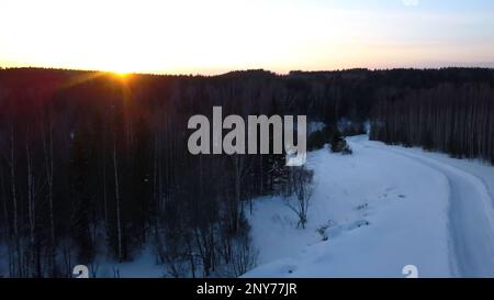 Veduta aerea di una motoslitta che percorre la pineta. Fermo. Cielo tramonto e strada rurale coperta di neve Foto Stock