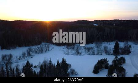 Veduta aerea di una motoslitta che percorre la pineta. Fermo. Cielo tramonto e strada rurale coperta di neve Foto Stock