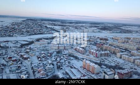 Vista aerea di una grande città con tetti coperti di neve. Fermo. Volare sopra città ghiacciata e un fiume Foto Stock