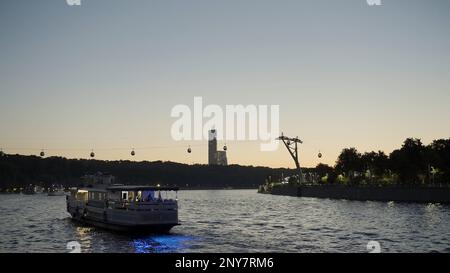 Paesaggio al tramonto con uno yacht turistico che naviga lungo l'argine. Azione. Funivia che si sposta sopra il fiume Foto Stock