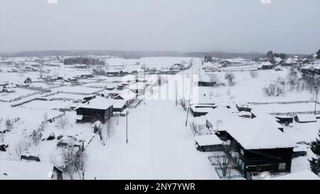 Vista aerea dei tetti innevati di case in legno. Fermo. Piccolo villaggio invernale su un cielo nuvoloso sfondo Foto Stock