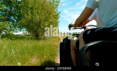 In quad lungo i campi. Fermo. Passeggiate lungo il sentiero di campagna vicino alla foresta e campo su uno sfondo cielo nuvoloso, stile di vita attivo Foto Stock