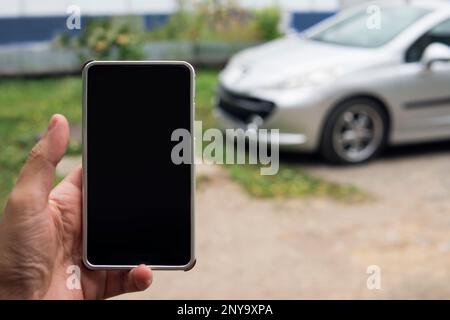 Man utilizza l'applicazione telefono per avviare automaticamente il veicolo. Smartphone con schermatura vuota in mano maschile utilizzato per sbloccare l'auto. Collegamento tra o Foto Stock