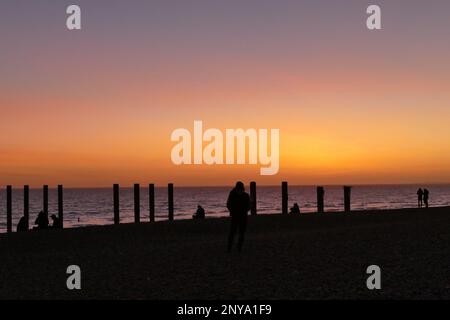 Un gruppo di persone che ammirano il pittoresco tramonto mentre splende su una spiaggia luminosa Foto Stock