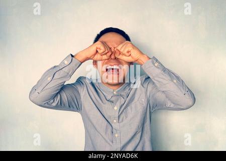 un ragazzo pazzo che piange. Un uomo cresciuto in una camicia blu urla e grida. Emozione negativa. Le persone reagiscono negativamente ai problemi. Foto Stock