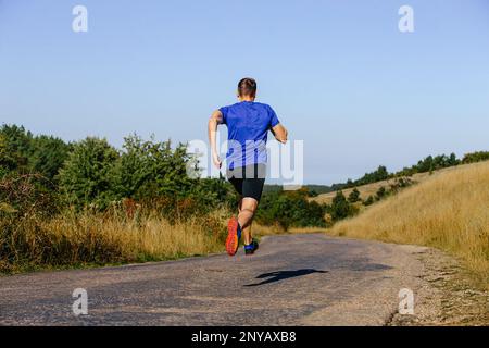 corridore maschio posteriore che corre su strada in pianura Foto Stock